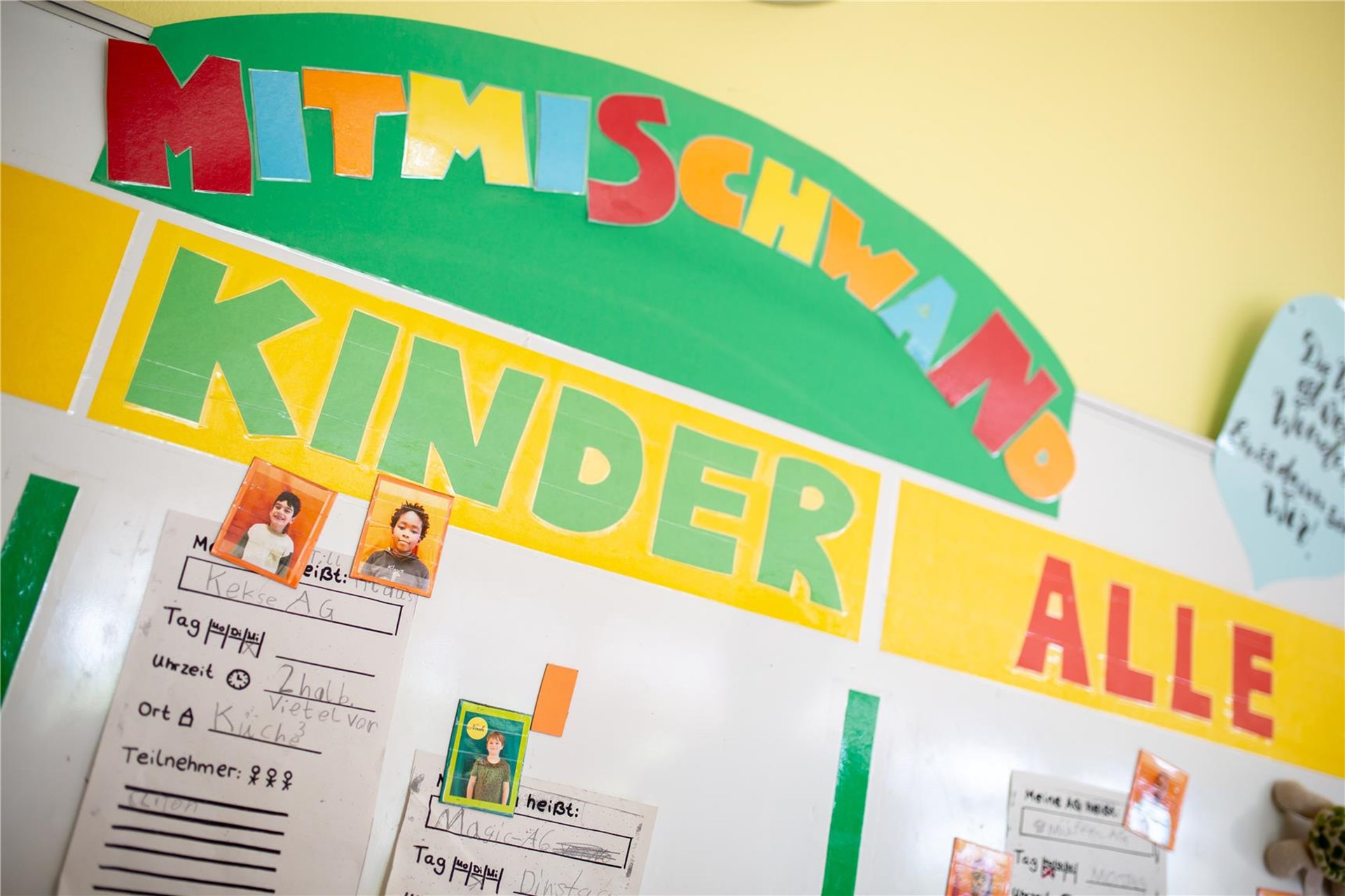 Eine ansprechende Pinnwand in einem Kindergarten zeigt die Aufschrift "Mitmisch-Kinder alle".  Diverse Fotos von Kindern und Notizen sind auf der Tafel befestigt.